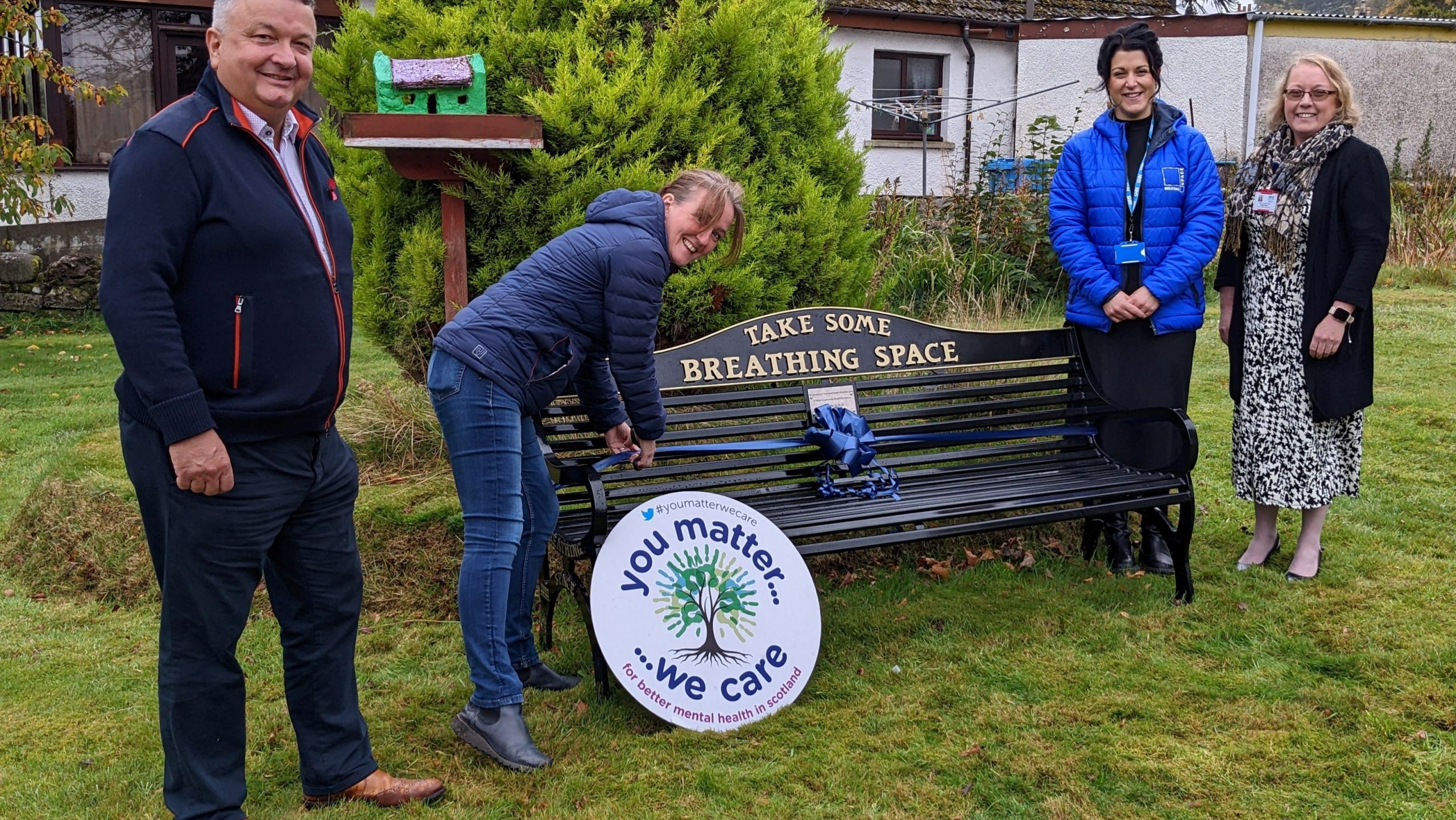 4 people standing smiling around bench